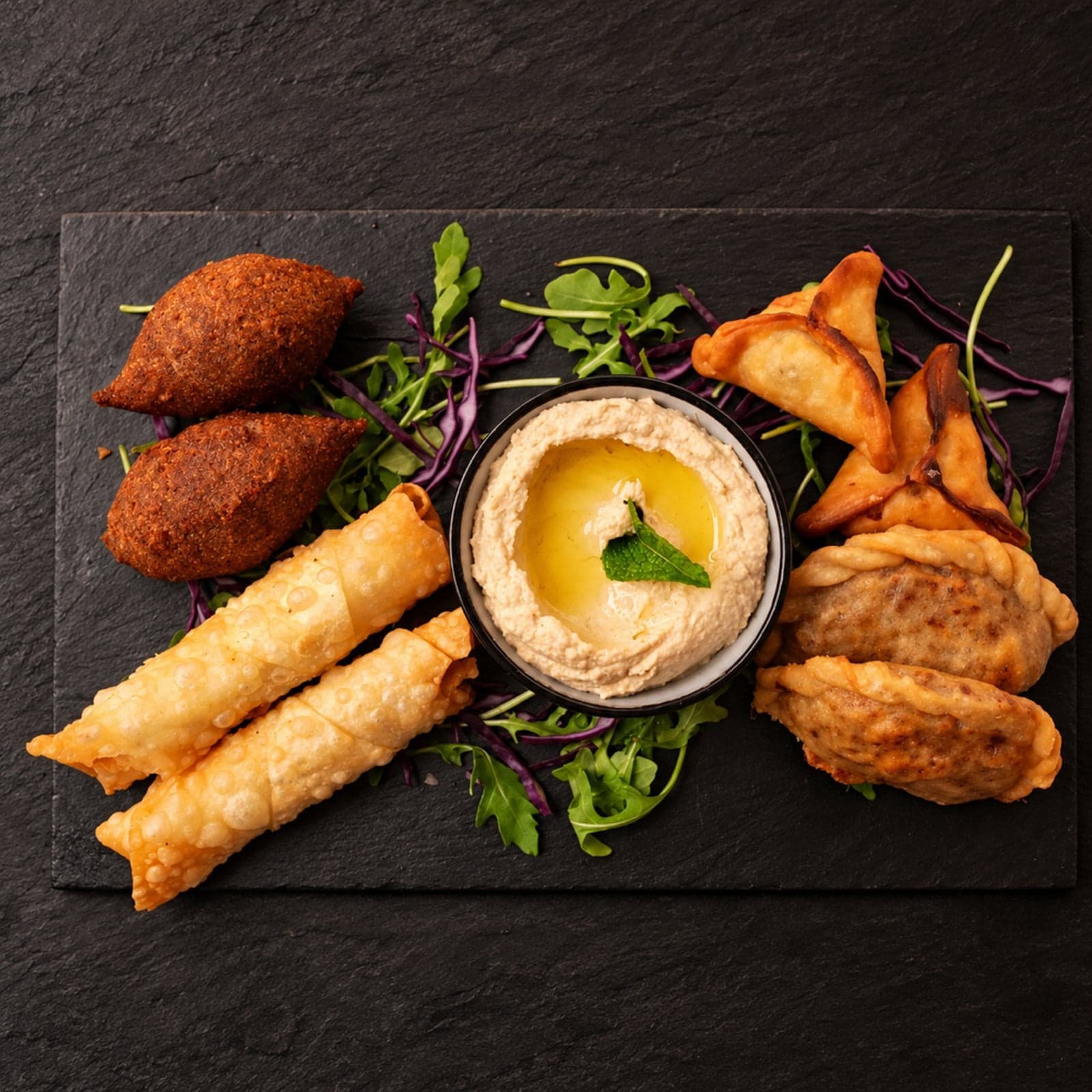 Un plateau de mezza libanais sur ardoise : kebbé, cigares au fromage, houmous et sambousek