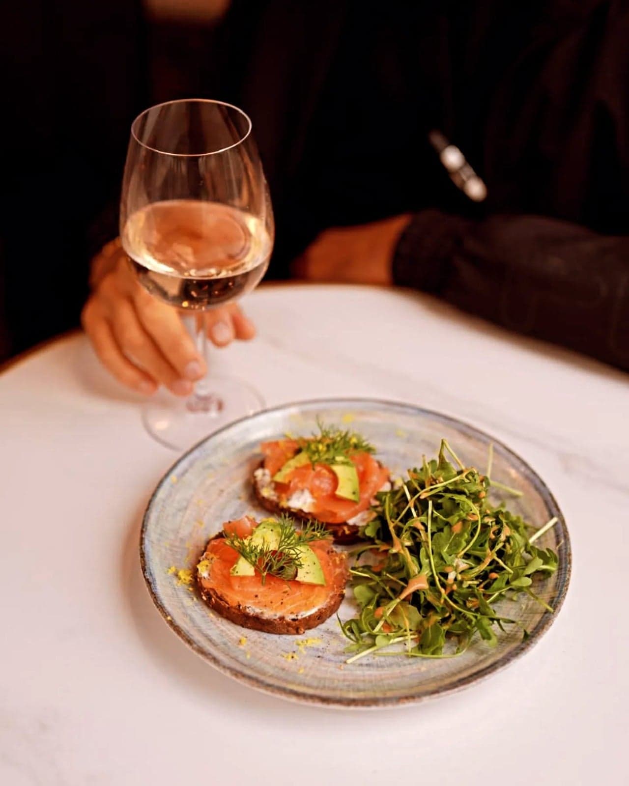 Deux tartines de saumon fumé et d'avocat, servies avec une salade et un verre de rosé
